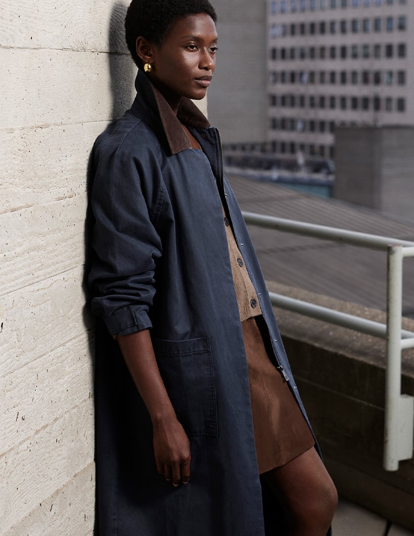 Woman wearing Whistles navy long coat with brown collar styled with brown suede skirt and gold earrings now 20% off.