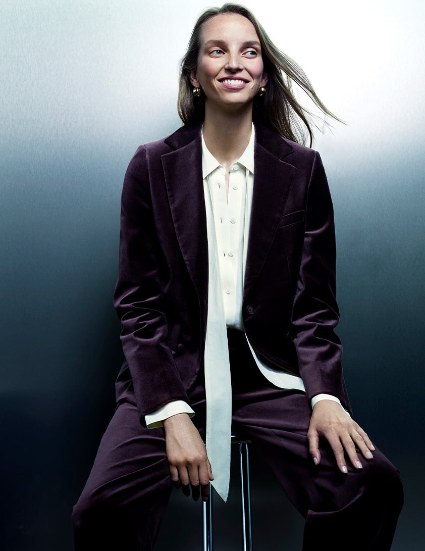 Woman wearing a Whistles purple velvet blazer with matching tailored trousers, layered over a white button-down shirt