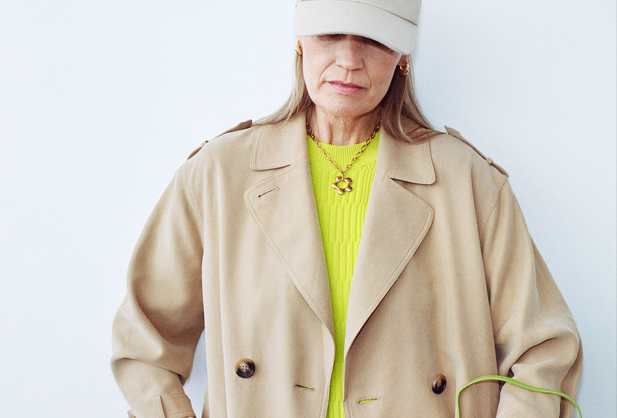 woman waeing a basball cap and neon yelllow dresss and tan trench coat