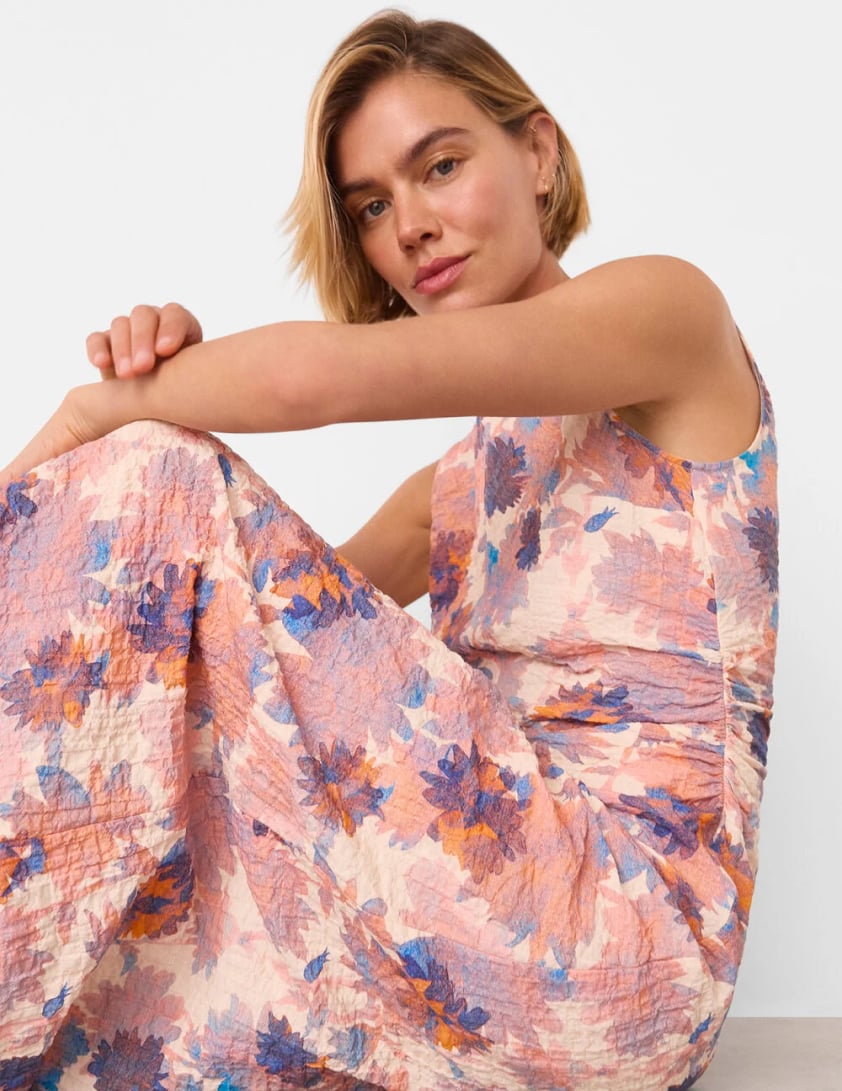 Woman wearing a sleeveless textured pink and purple floral dress sitting with legs folded for Whistles 15% off everything promotion