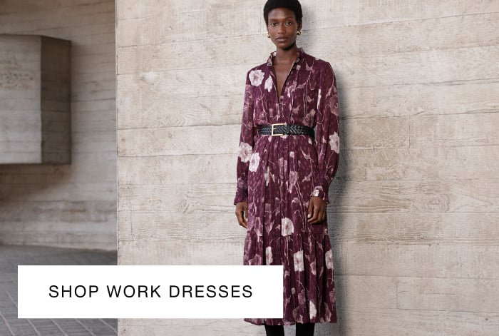 Woman wearing Whistles' purple floral midi dress with a V-neck and long sleeves, styled with a black woven belt and black suede boots
