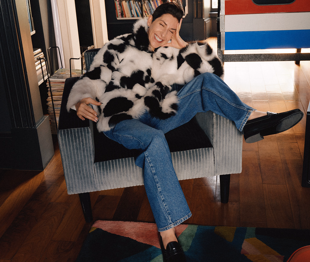 Model sitting on a bench in a cow-print Cookies & Cream coat and straight-leg jeans