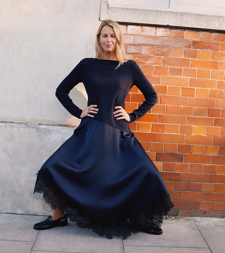 Model against a brick wall in a navy satin lace-trim midi dress