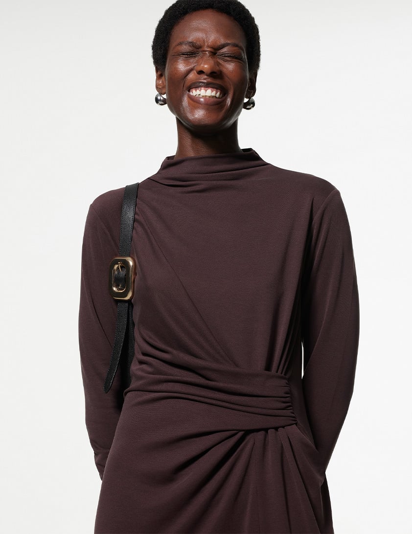 Woman wearing Whistles' chocolate-brown maxi dress with a twist-ruched waist, long sleeves, and a black leather shoulder bag