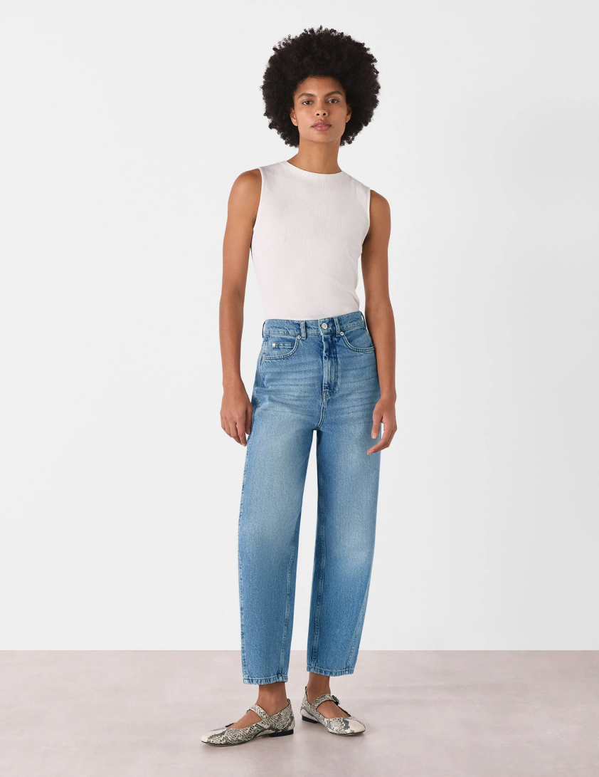 Woman wearing a sleeveless white top with high waisted wide leg light blue jeans for Whistles 15% off everything promotion