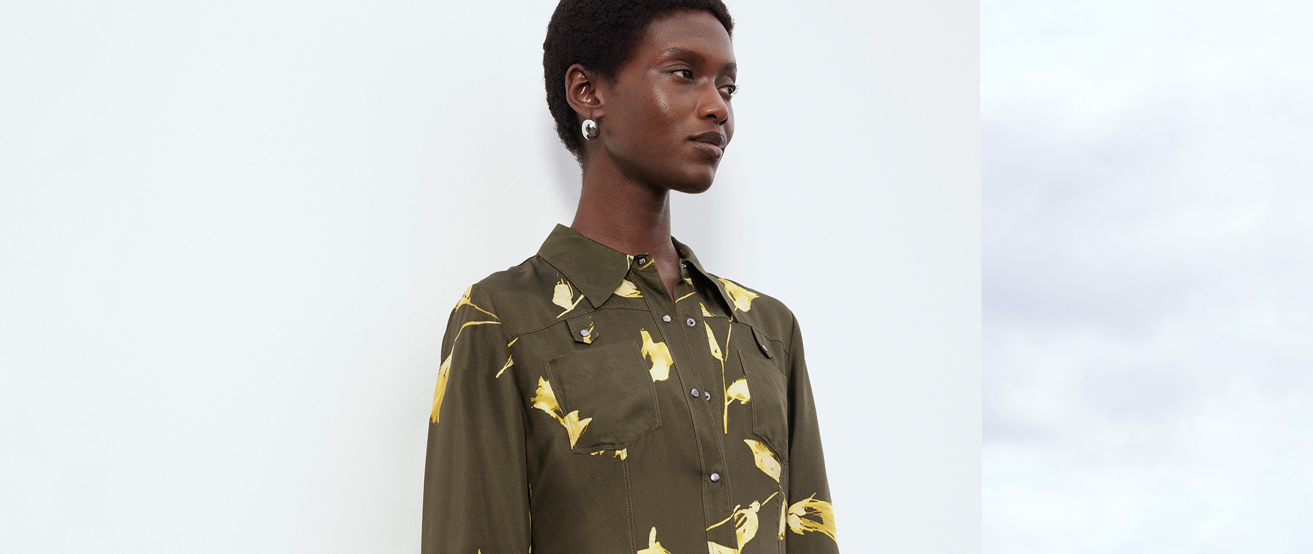 Model wearing Whistles Limited Edition AW25 collection olive green shirt dress with yellow floral print, modern minimalist design