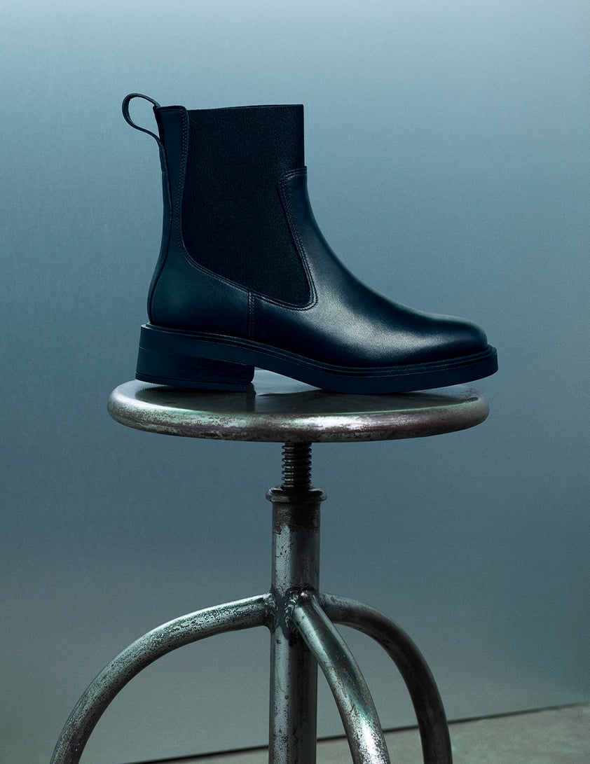 Whistles black leather ankle boots for women, Chelsea style with elasticated side panels and pull tab, shown on stool