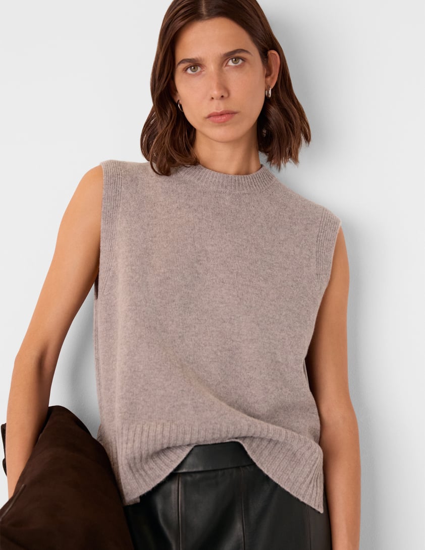Model wearing Whistles sleeveless taupe knit top with black leather skirt, holding a chocolate suede bag now 20% off